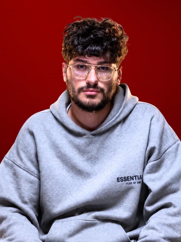 Alireza Firouzja in glasses and a grey hoodie, against a red studio backdrop