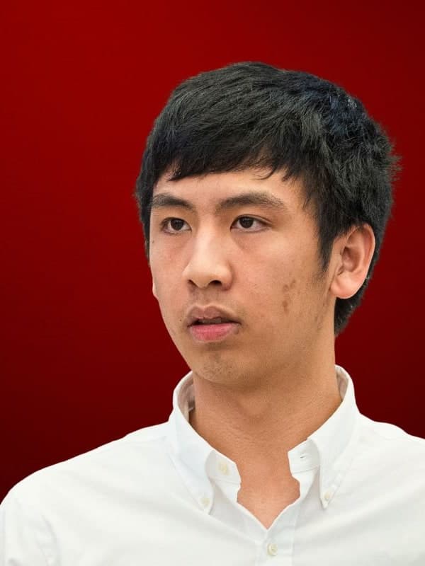 Andrew Hong in a white open-collar shirt, looking to one side, against a red studio backdrop
