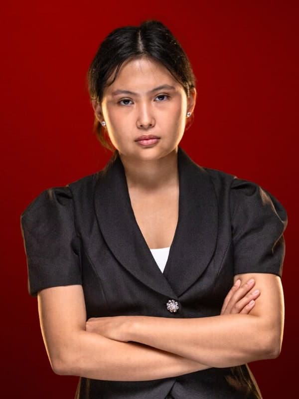 Bibisara Assaubayeva in a black jacket, arms folded, against a red studio backdrop