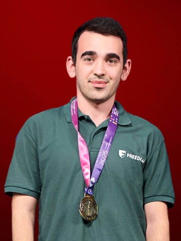 Haik M. Martirosyan in a green polo shirt, wearing a medal, against a red studio backdrop