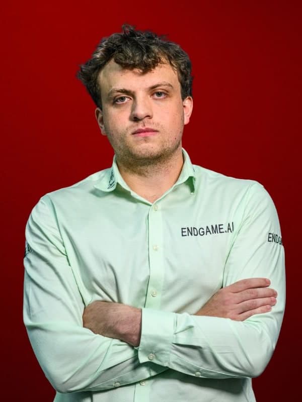 Hans Moke Niemann in a pale green shirt, arms folded, against a red studio backdrop