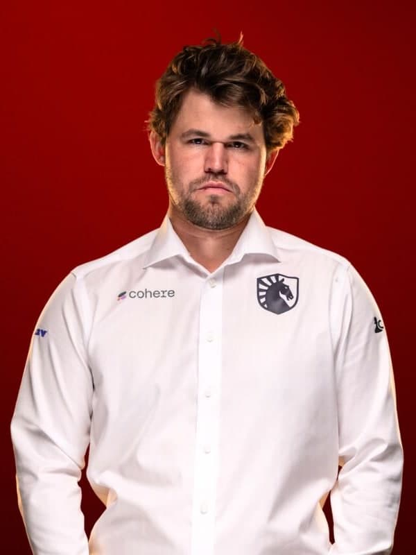 Magnus Carlsen in a white team shirt, arms folded, against a red studio backdrop