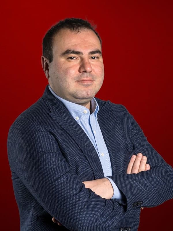 Shakhriyar Mamedyarov in a navy blazer, arms folded, against a red studio backdrop