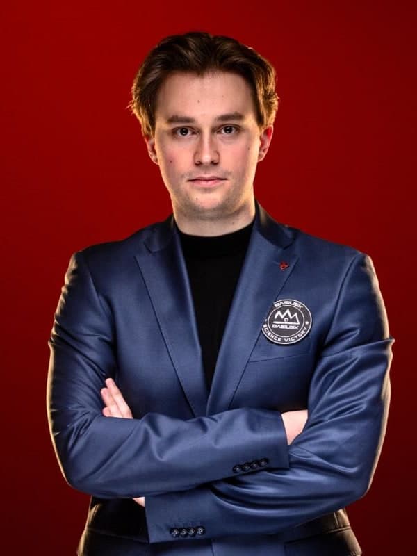 Vincent Keymer in a navy blazer, arms folded, against a red studio backdrop